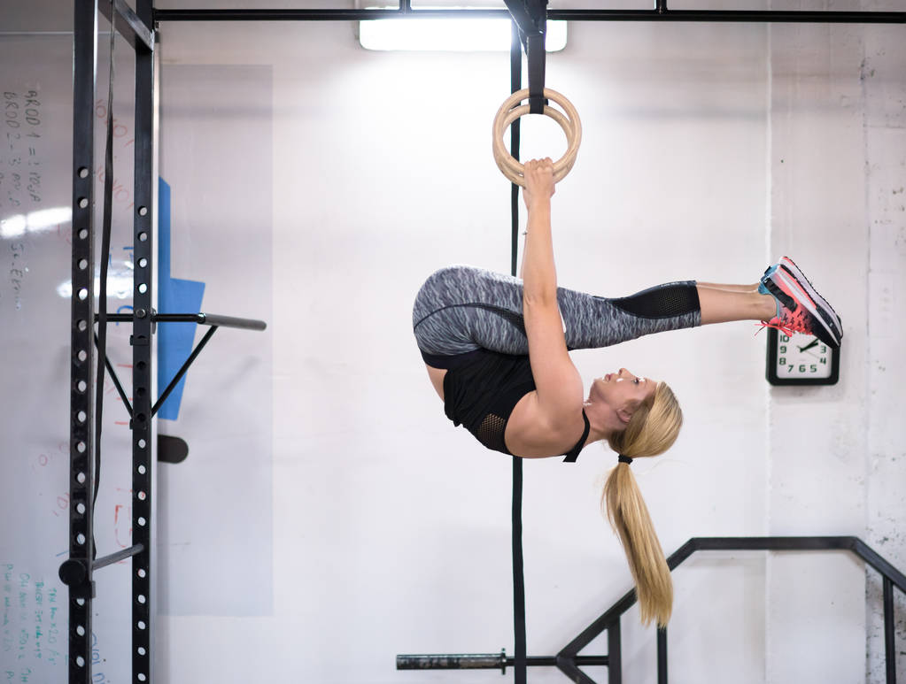 junge athletische Frau turnt in der Crosslaufhalle an den Ringen - Foto, Bild