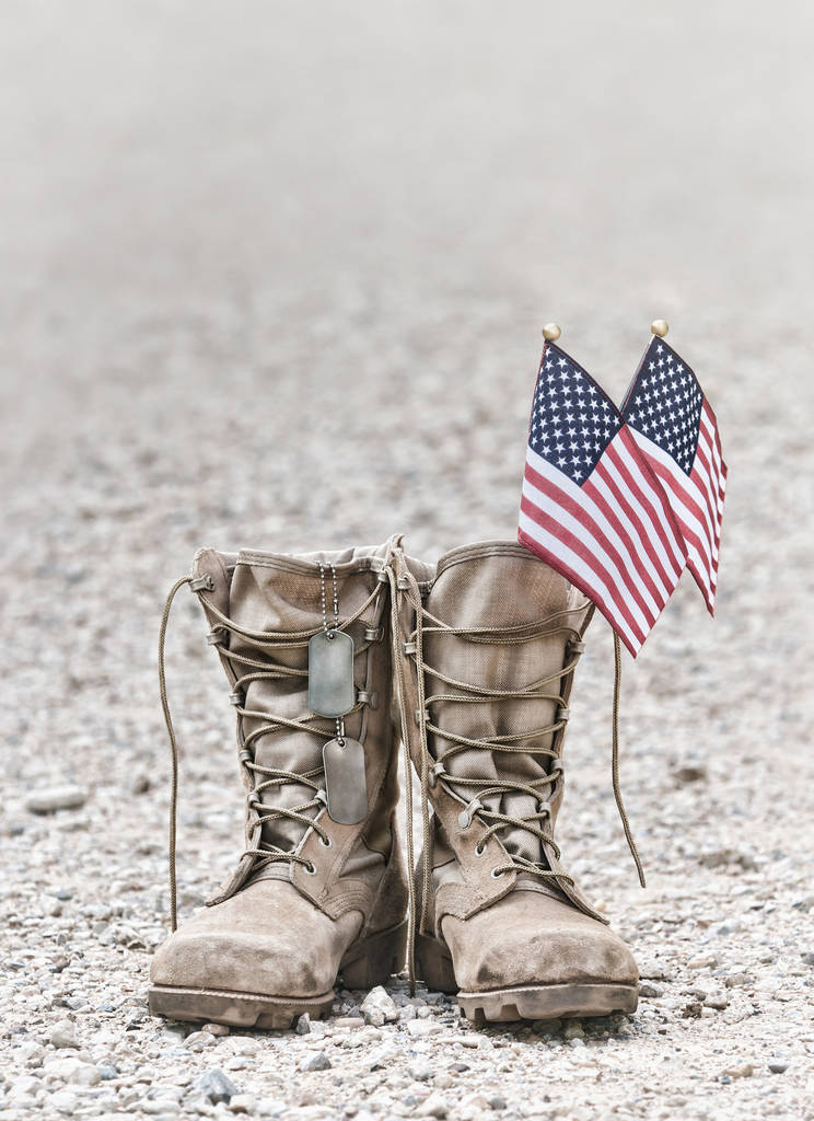 Oude militaire bestrijden laarzen met markeringen van de hond en twee kleine Amerikaanse vlaggen. De achtergrond van de rotsachtige grind met kopie ruimte. Memorial Day of Veterans day concept. Vintage Toon. - Foto, afbeelding