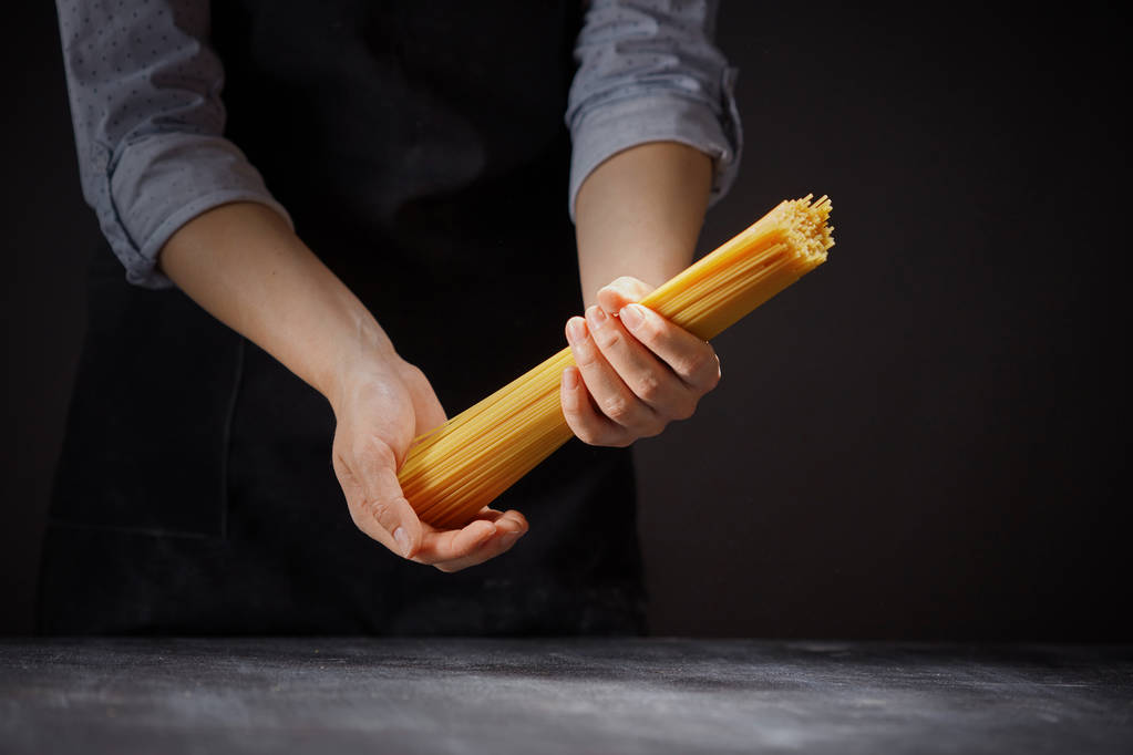 el manojo de los espaguetis en las manos de la mujer sobre el fondo oscuro, el concepto de la comida italiana
 - Foto, imagen