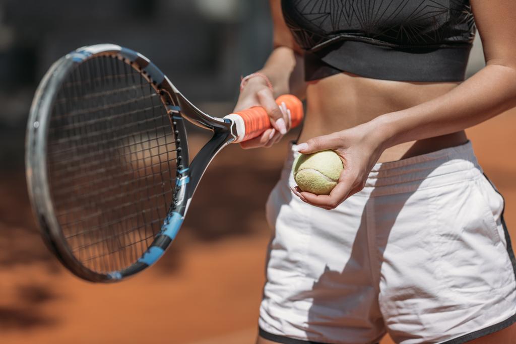 Oříznout záběr sportovní mladé ženy s tenisovou raketu a míček - Fotografie, Obrázek
