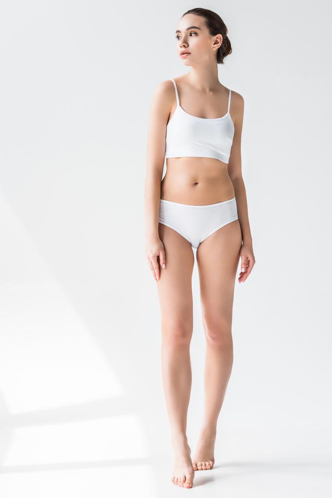 jovem atraente mulher caucasiana em lingerie branca olhando para longe isolado no fundo cinza
  - Foto, Imagem