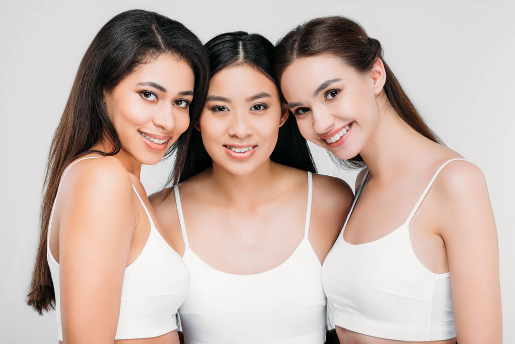 счастливые мультикультурные девушки, позирующие в белых бюстгальтерах, изолированные на сером
 - Фото, изображение