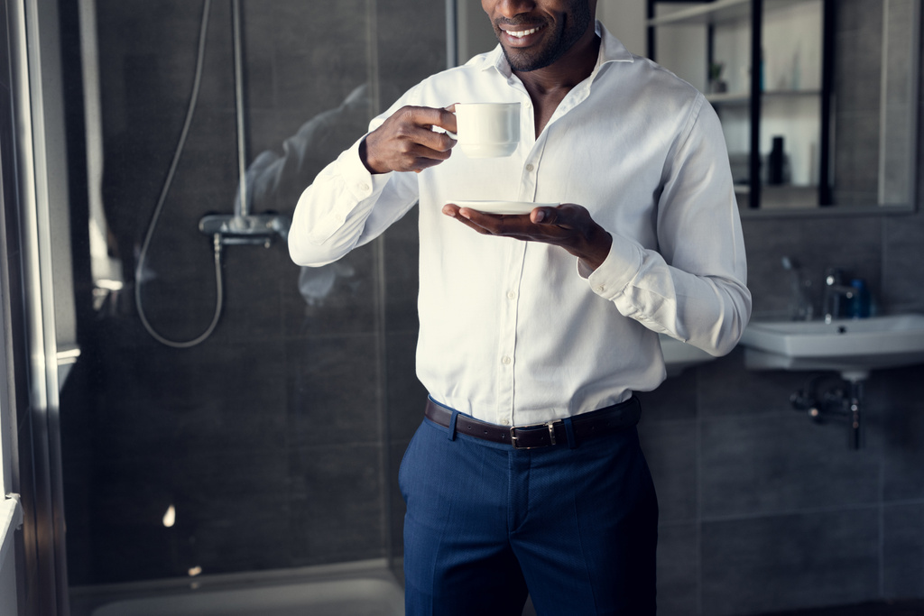 όμορφος νεαρός επιχειρηματίας σε λευκό πουκάμισο πίνει καφέ στο μπάνιο - Φωτογραφία, εικόνα