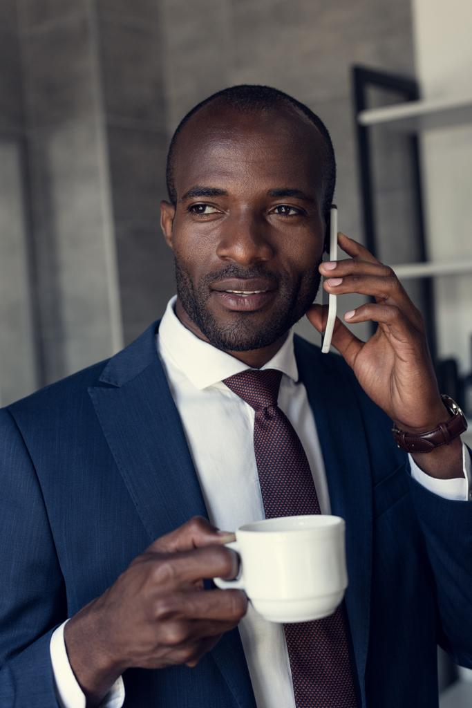 thoughtful young businessman with cup of coffee talking by phone - Photo, Image