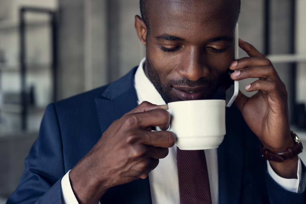 Nahaufnahme eines gut aussehenden jungen Geschäftsmannes mit einer Tasse Kaffee im Telefongespräch - Foto, Bild