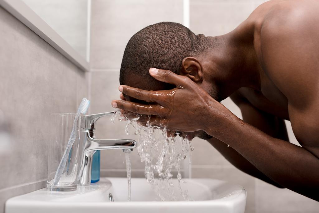 vista lateral del joven lavándose la cara en el baño por la mañana
 - Foto, imagen