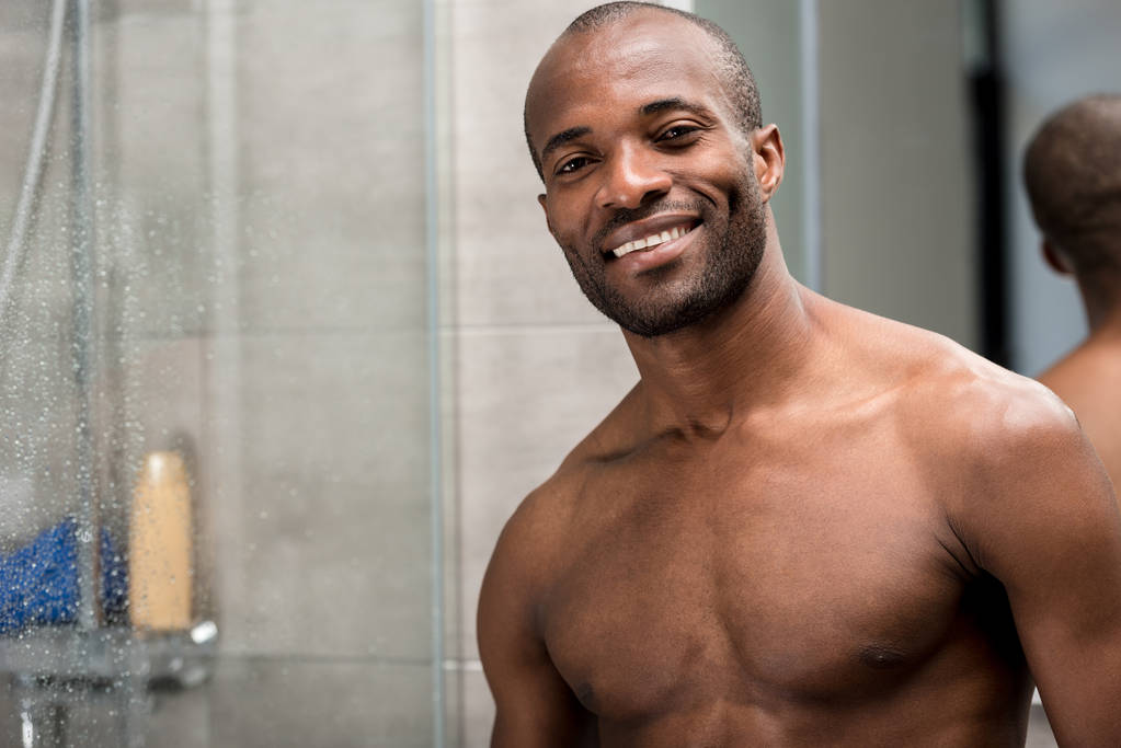 komea paljain rinnoin afrikkalainen amerikkalainen mies seisoo kylpyhuoneessa ja hymyilee kameralle
 - Valokuva, kuva