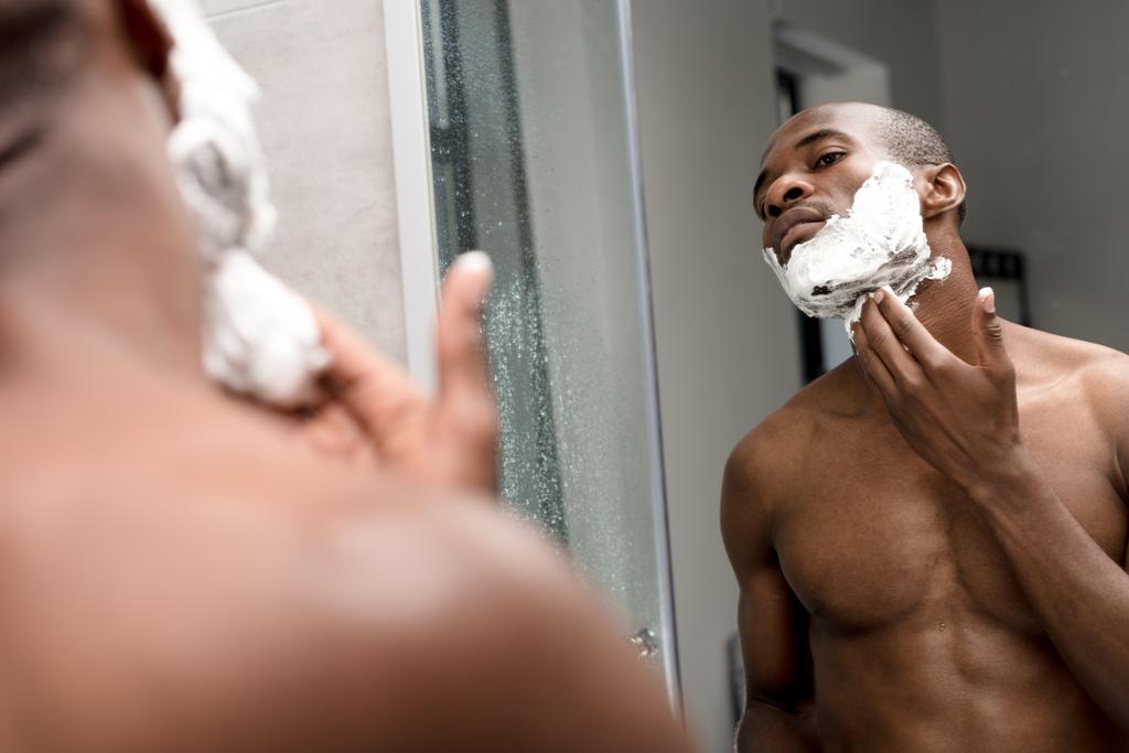 обрезанный снимок красивого африканского американца, бреющегося и смотрящего в зеркало
 - Фото, изображение