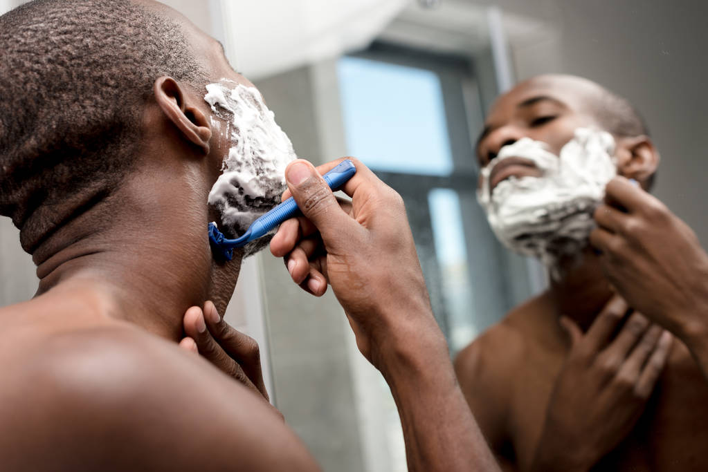 επιλεκτική εστίαση όμορφος αφρικανική αμερικανική άνδρα ξύρισμα και κοιτάζοντας καθρέφτη - Φωτογραφία, εικόνα