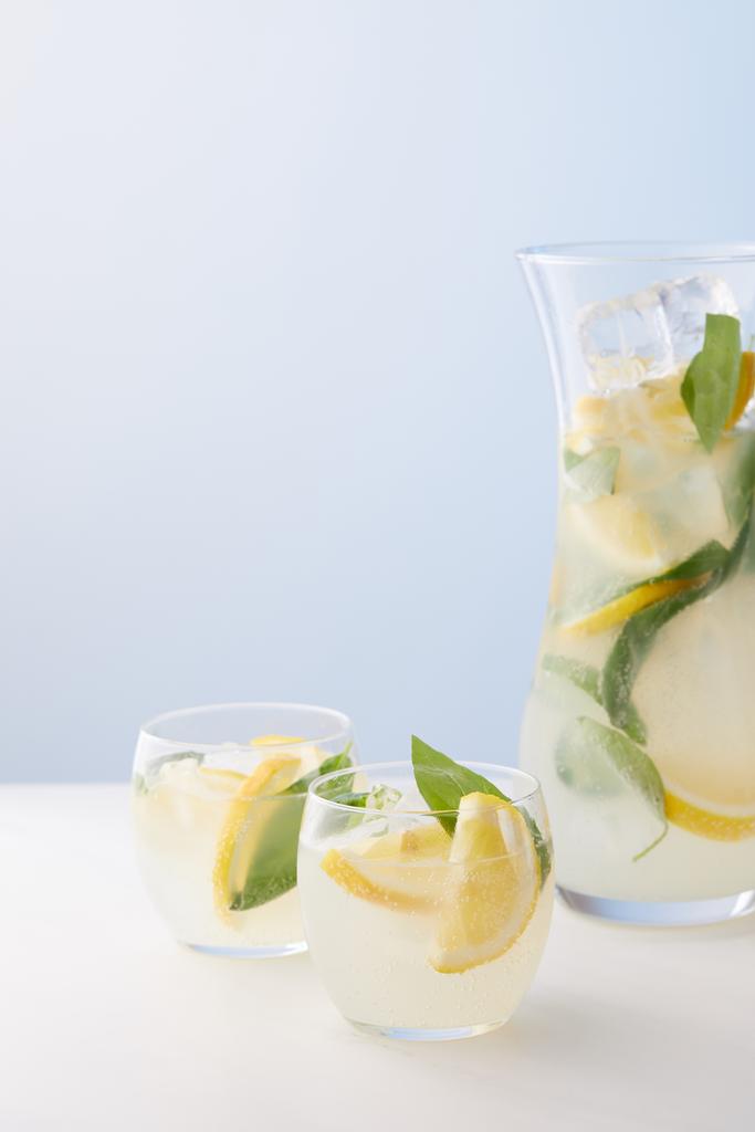  水差し、レモネードとミントの葉、氷とレモン スライスを青い背景の 2 つのグラス  - 写真・画像