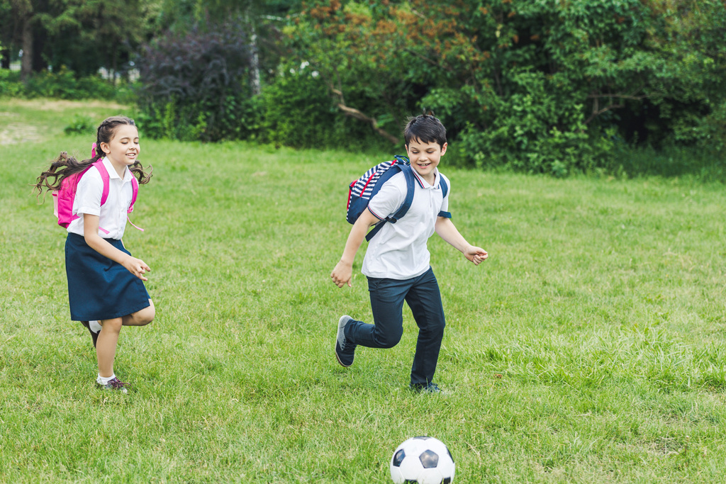 écoliers avec sacs à dos jouant au football ensemble sur prairie dans le parc
 - Photo, image
