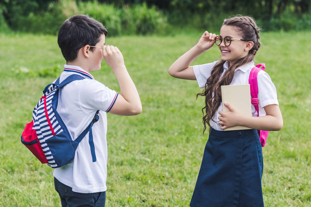 adorable schoolchildren with backpacks looking at each other through eyeglasses - Photo, Image
