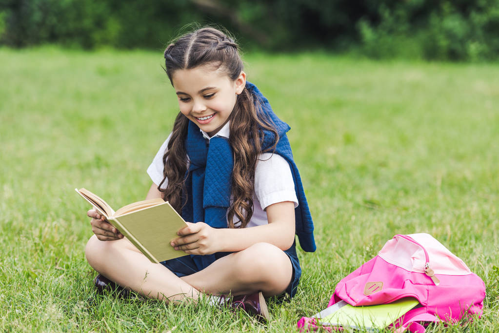 boldog iskolás olvasó a könyvet, a fű a parkban ülve - Fotó, kép