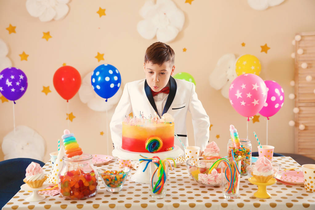Schattige kleine jongen uitblazen van de kaarsjes op zijn verjaardagstaart binnenshuis - Foto, afbeelding
