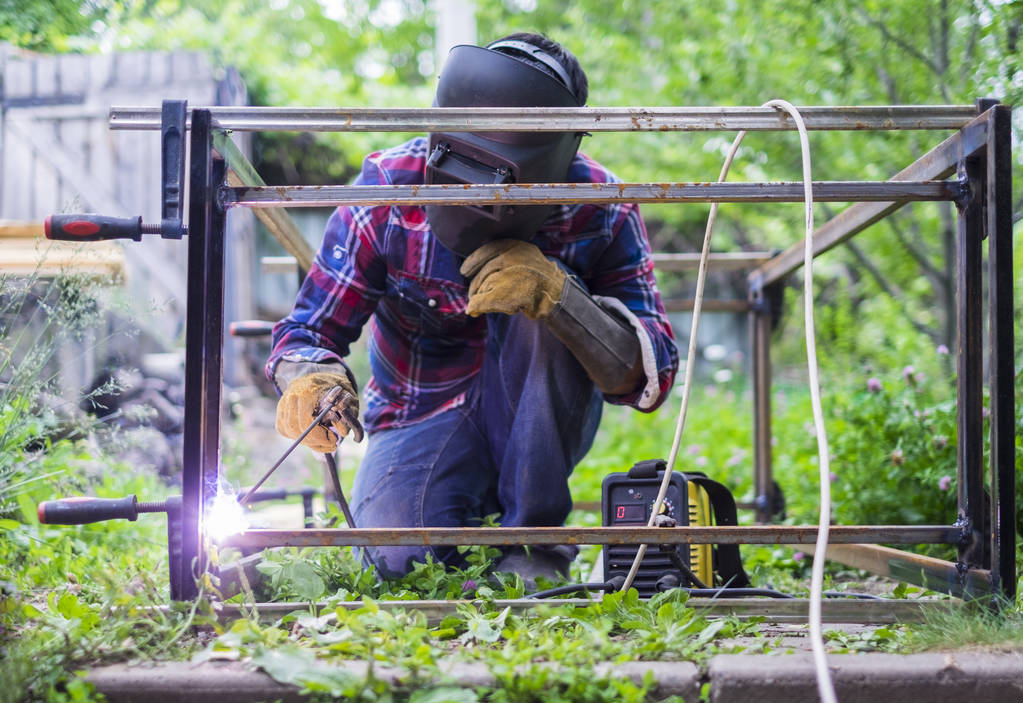 Homem em uma máscara protetora soldagem construção de metal fora em um dia de verão
. - Foto, Imagem