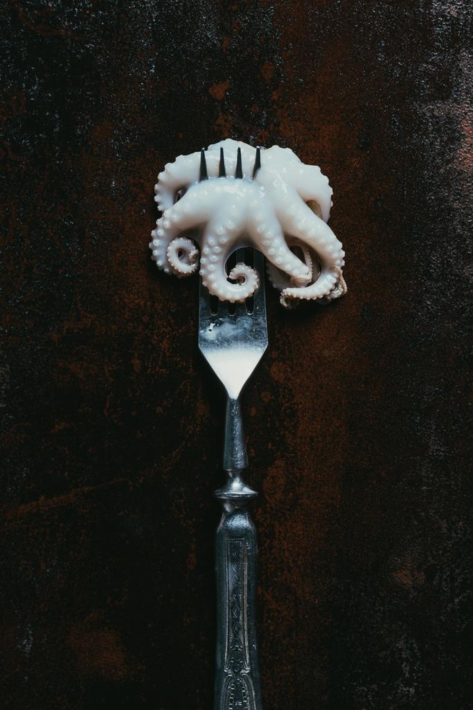 top view of little raw octopus on fork on rusty metal surface - Photo, Image