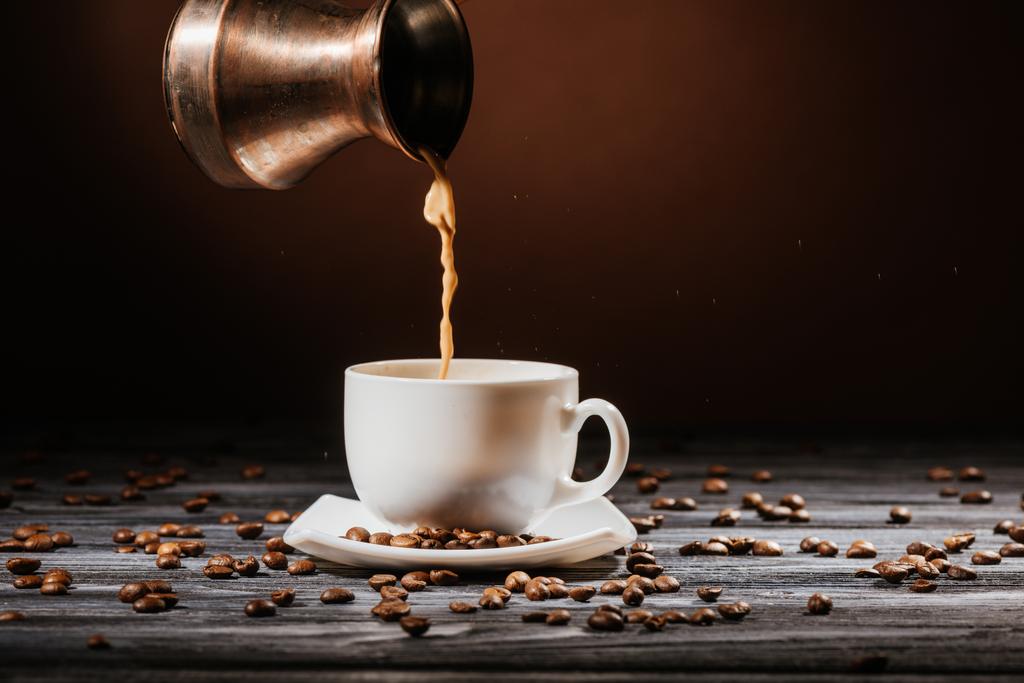 Nahaufnahme von Kaffee, der aus Cezve in Tasse auf rustikalem Holztisch gegossen wird - Foto, Bild