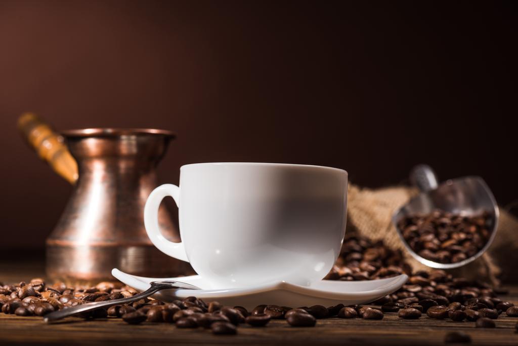 Close-up shot van kopje koffie met geroosterde bonen en vintage cezve op donkere bruine achtergrond - Foto, afbeelding