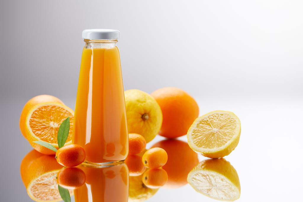 garrafa de suco fresco com laranjas, limões e kumquats na superfície reflexiva
 - Foto, Imagem