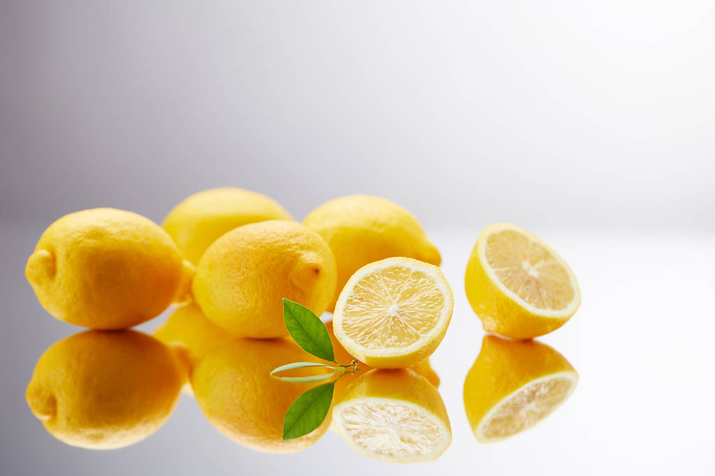 κοντινή λήψη ενός μάτσο φρέσκα λεμόνια στην αντανακλαστική επιφάνεια και σε γκρι - Φωτογραφία, εικόνα