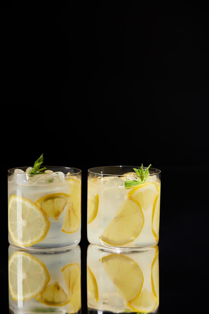 glasses of delicious fresh lemonade on reflective surface isolated on black - Photo, Image