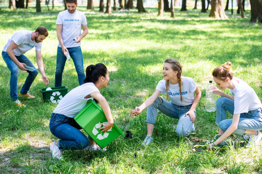 молодые волонтеры с коробками для переработки чистки газона в парке
 - Фото, изображение