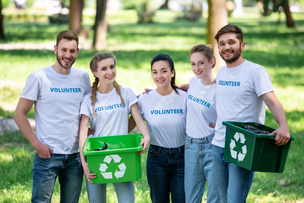 jóvenes voluntarios con cajas de reciclaje verdes para la basura de pie en el parque
  - Foto, imagen