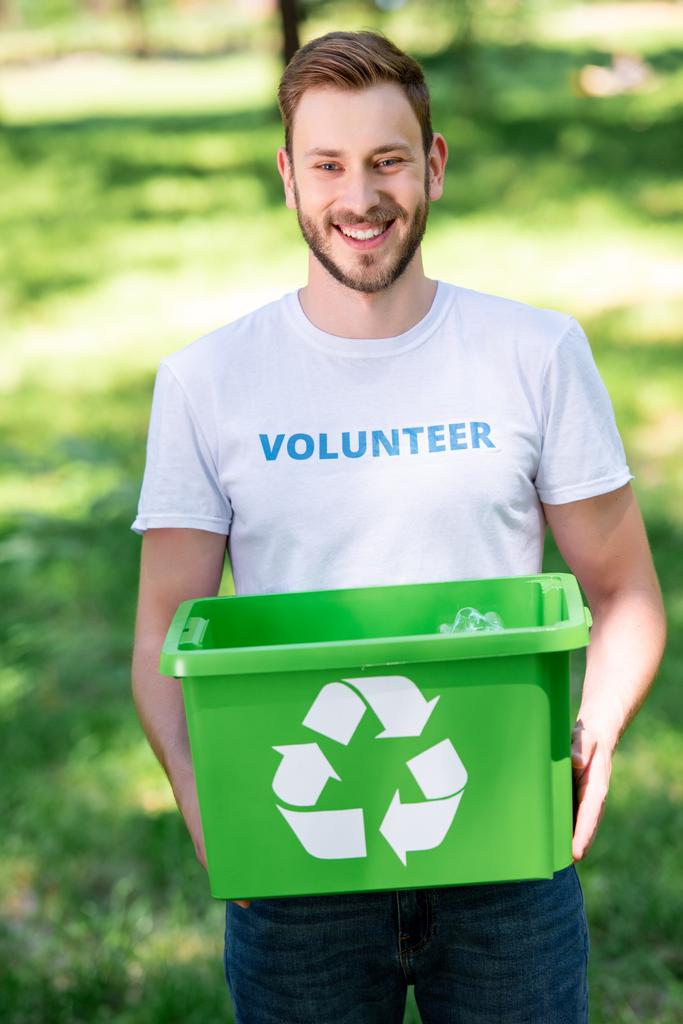 Sourire volontaire masculin tenant boîte de recyclage avec des ordures dans le parc
 - Photo, image