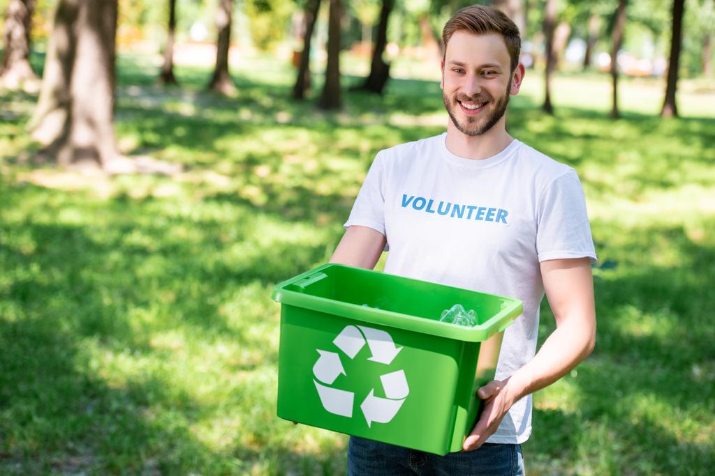 Lächelnder Freiwilliger hält Recyclingbox mit Plastikmüll in der Hand - Foto, Bild
