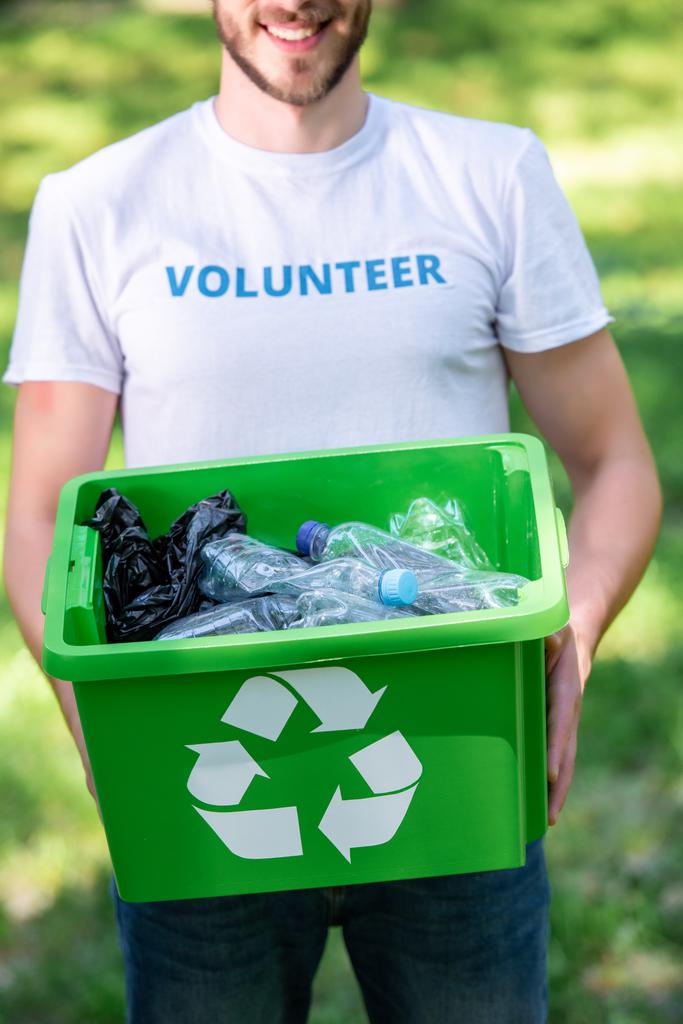 częściowy widok uśmiechający się wolontariusz gospodarstwa pudełko z odpadów z tworzyw sztucznych recykling - Zdjęcie, obraz