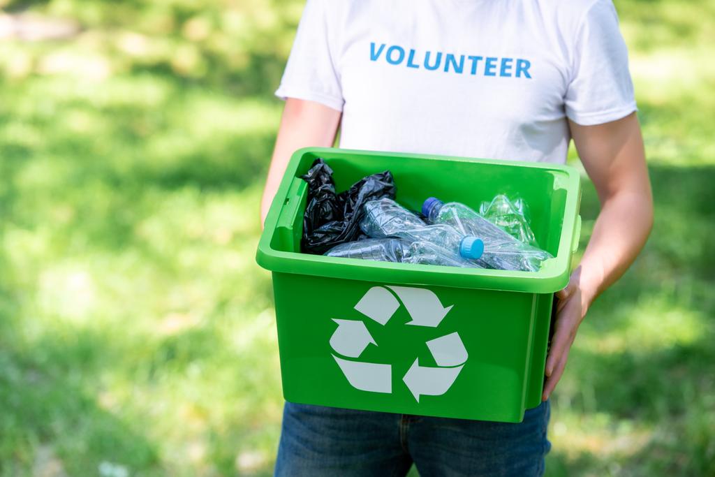 vista parcial de un voluntario varón sosteniendo una caja de reciclaje con residuos plásticos
 - Foto, imagen