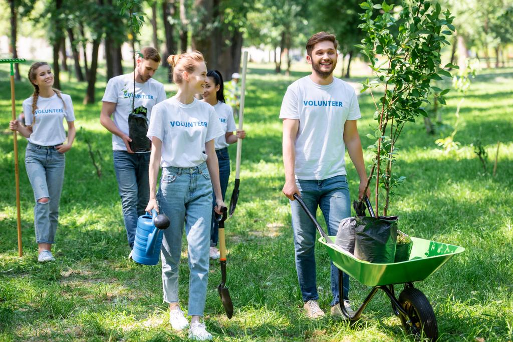 Счастливые друзья вместе занимаются волонтерством и высаживают деревья в парке
 - Фото, изображение