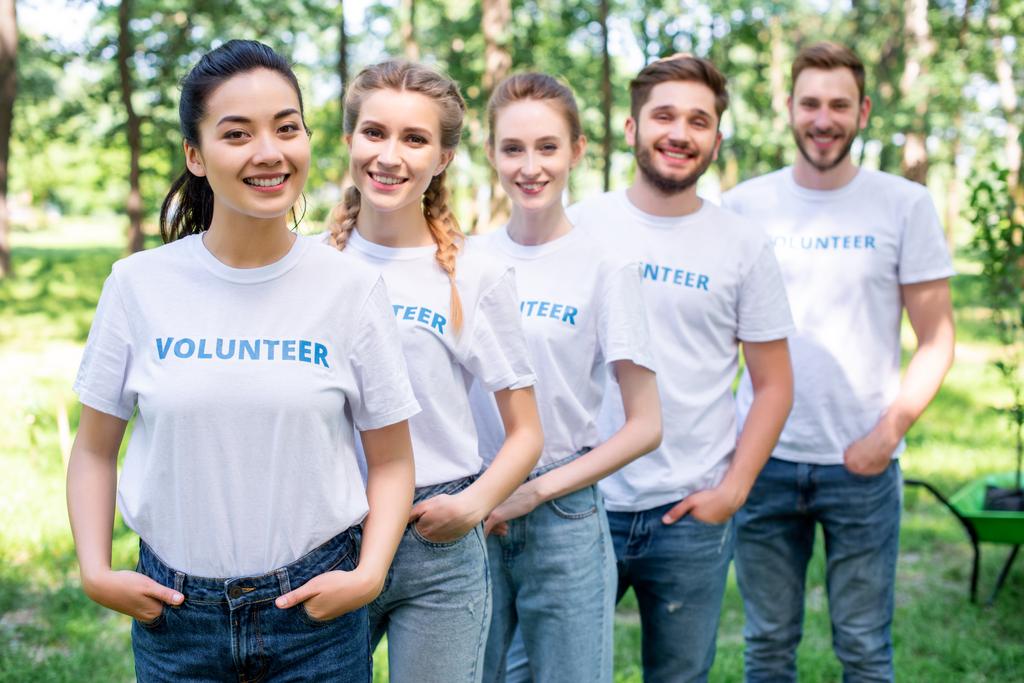 jóvenes voluntarios sonrientes de pie en fila en el parque
  - Foto, Imagen