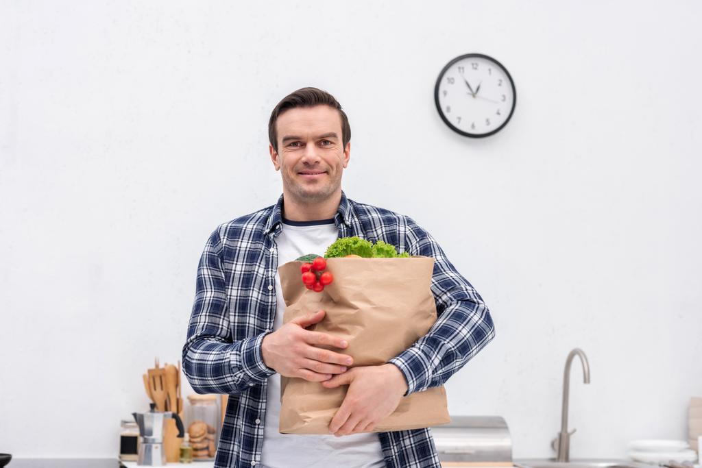 felice uomo adulto che trasporta borsa negozio di alimentari in cucina e guardando la fotocamera
 - Foto, immagini