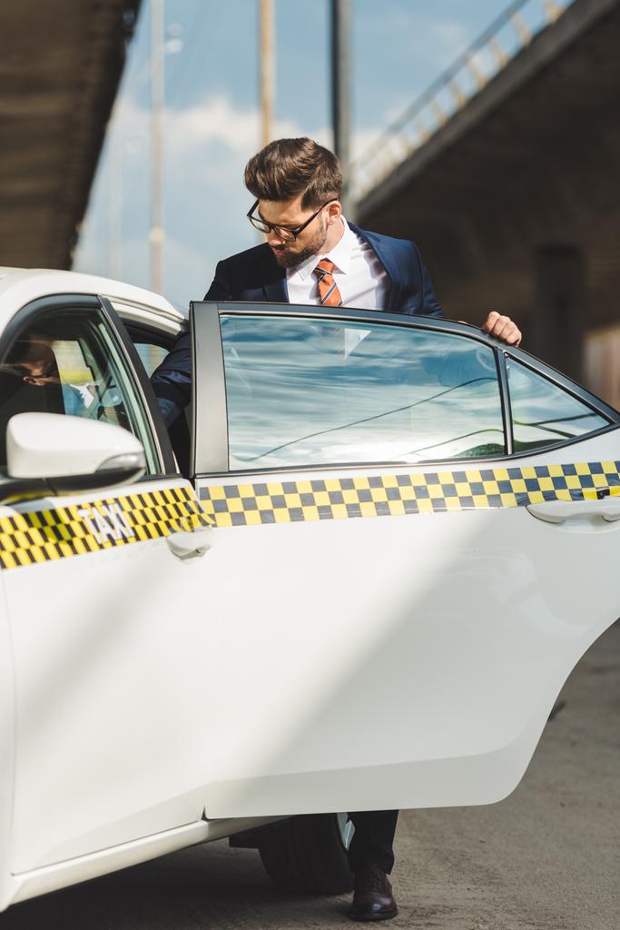 Красивый молодой человек в модном костюме и очках открывает дверь такси
  - Фото, изображение