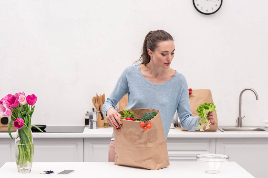 schöne erwachsene Frau nimmt Gemüse aus Papiertüte nach dem Einkaufen  - Foto, Bild