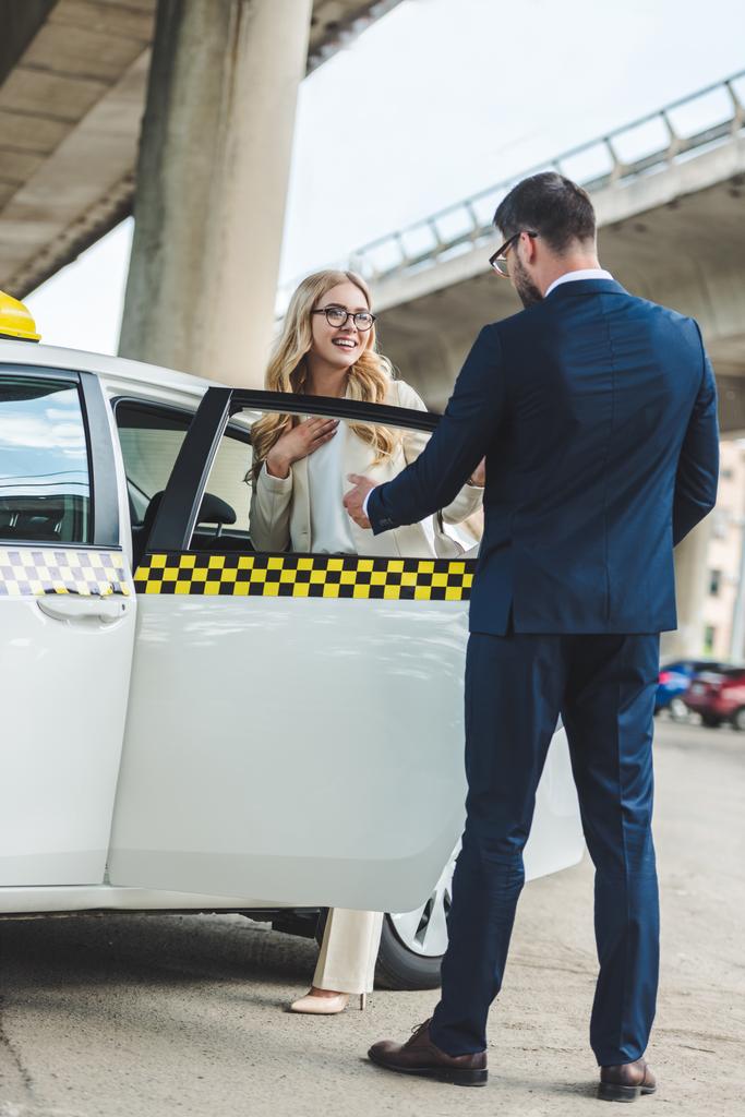 Mann im Anzug öffnet Autotür für schöne lächelnde Frau im Taxi - Foto, Bild
