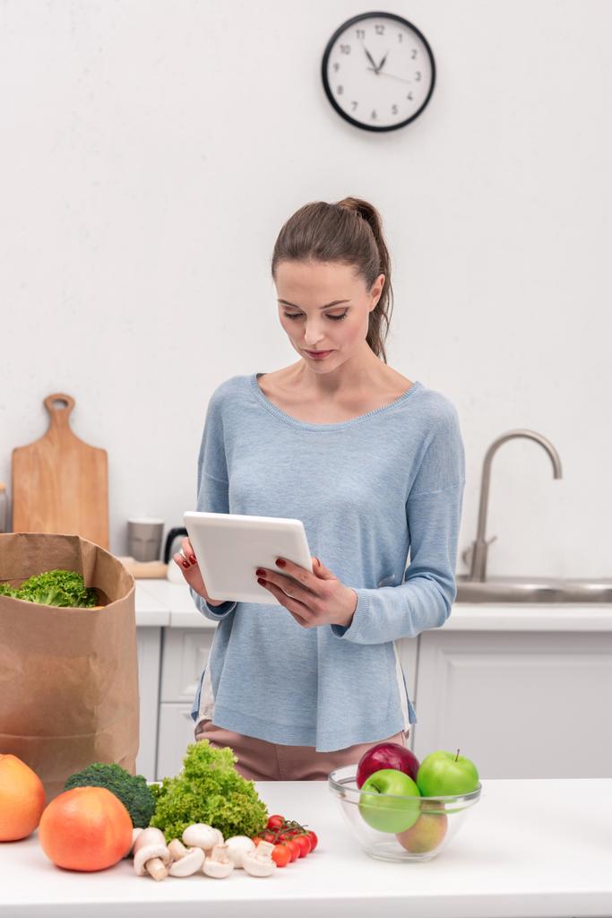 aantrekkelijke volwassen vrouw met tablet lijst van koopt na de boodschappen thuis te controleren - Foto, afbeelding
