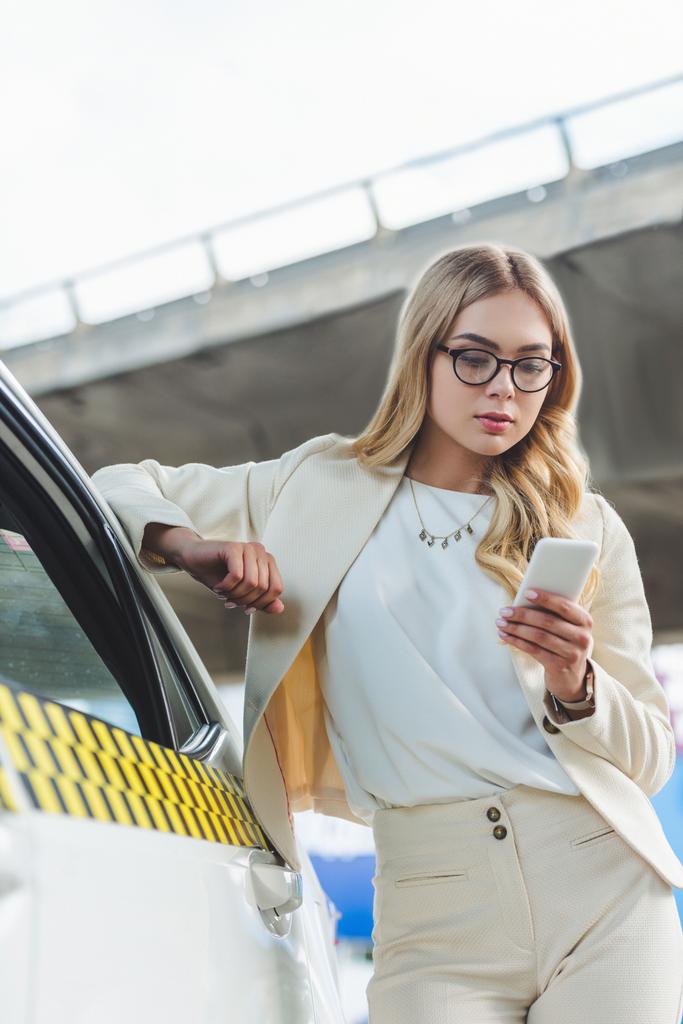 Taksi eğilerek ve smartphone kullanarak gözlük güzel sarışın kadın   - Fotoğraf, Görsel