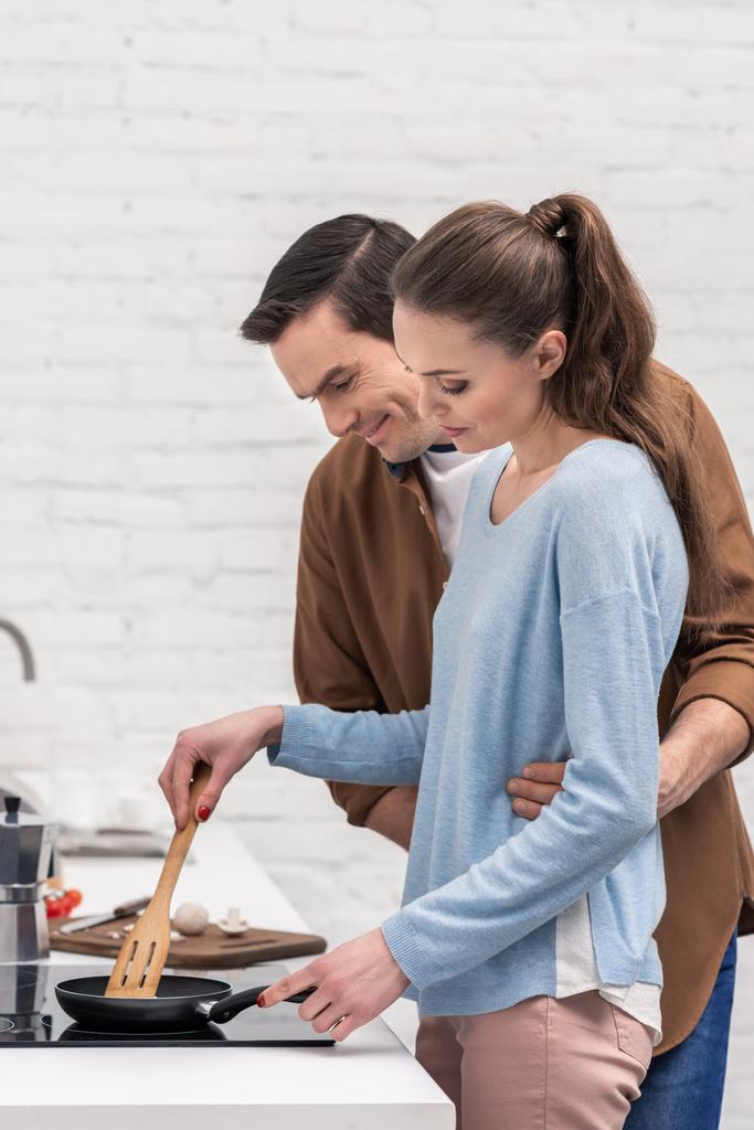 marido feliz abraçando sua esposa por trás enquanto ela cozinha
 - Foto, Imagem