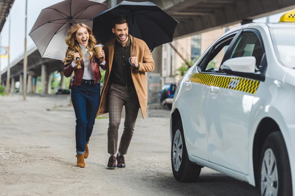 excitada pareja joven con paraguas corriendo juntos a taxi
 - Foto, Imagen