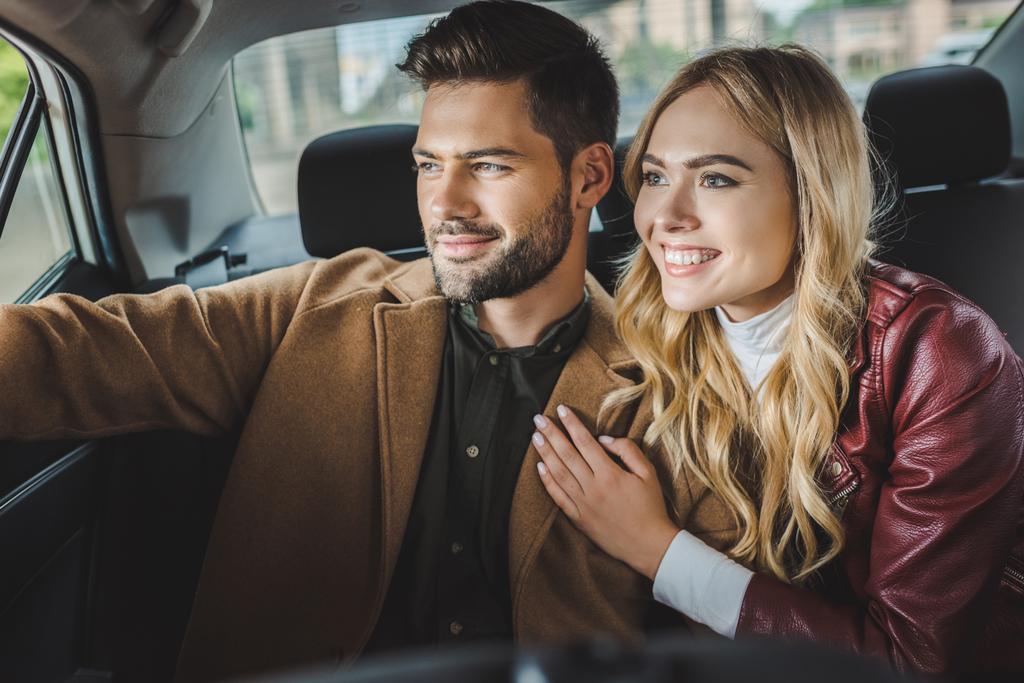 χαμογελώντας νεαρό ζευγάρι ψάχνει στο παράθυρο του αυτοκινήτου ενώ κάθονται μαζί στο ταξί - Φωτογραφία, εικόνα