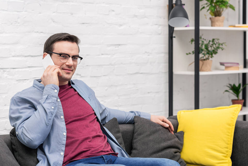 красивый взрослый мужчина разговаривает по телефону на диване дома
 - Фото, изображение