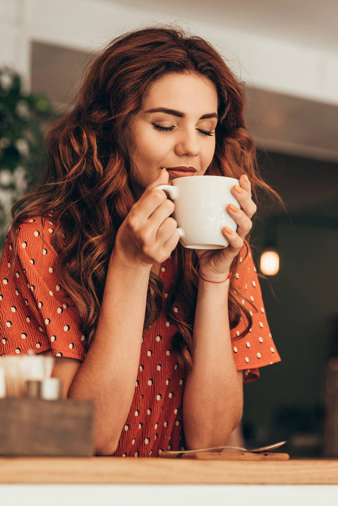 Porträt einer schönen Frau mit geschlossenen Augen, die eine Tasse aromatischen Kaffee in den Händen hält - Foto, Bild