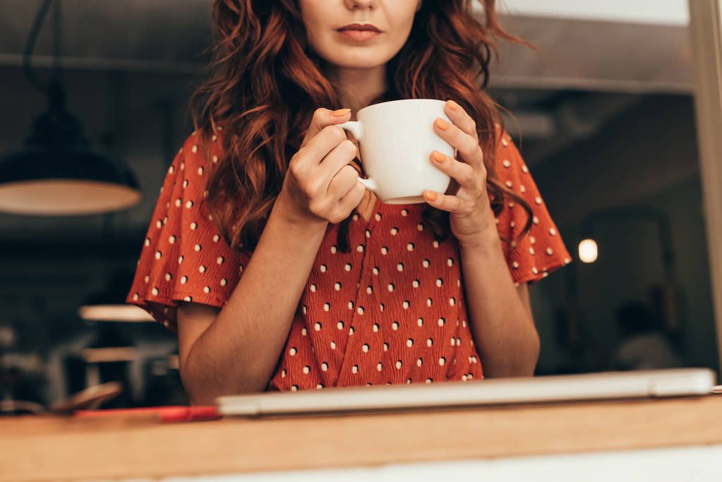 обрезанный снимок женщины с чашкой ароматного кофе в руках в кафе
 - Фото, изображение