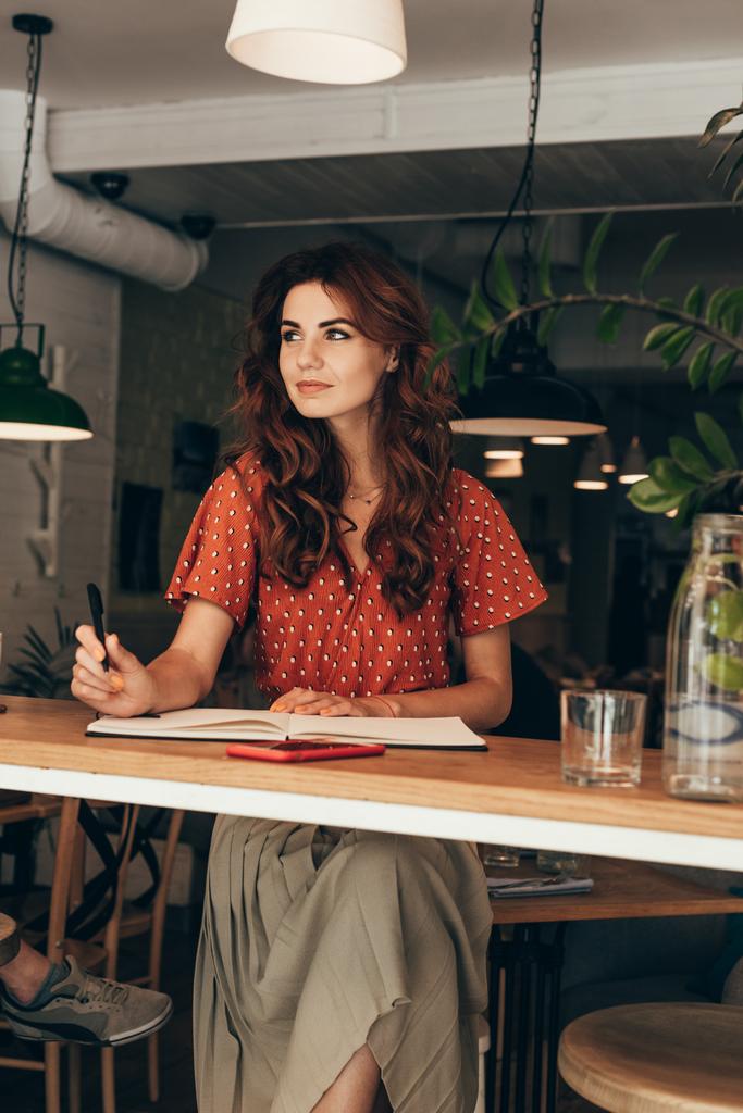 πορτρέτο του συλλογισμένος blogger που κάθεται στο τραπέζι με το σημειωματάριο στο κατάστημα καφέ - Φωτογραφία, εικόνα
