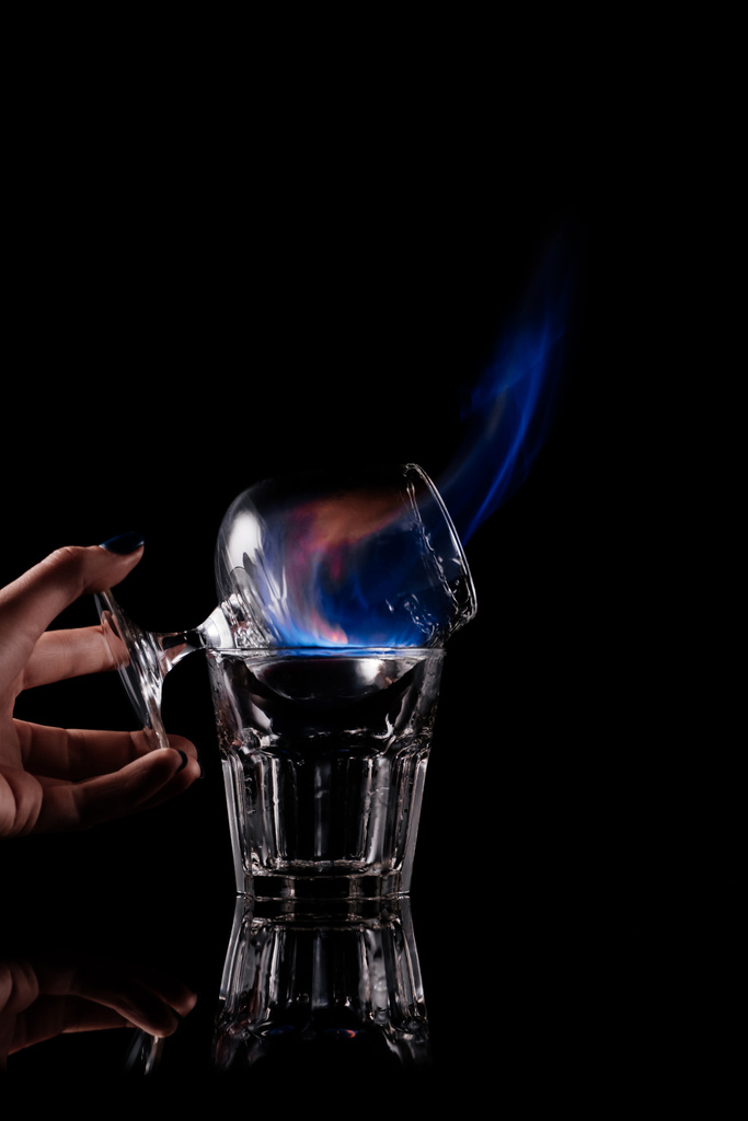 partial view of woman holding glass with burning sambuca alcohol drink on black background - Photo, Image