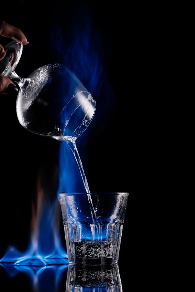 siyah arka plan üzerine yanan sambuca alkol içki cam içine dökme kadının kısmi görünümü - Fotoğraf, Görsel