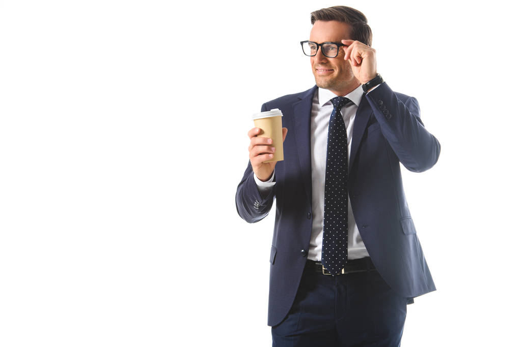 glimlachend zakenman aanpassen brillen en houden papieren kopje koffie geïsoleerd op witte achtergrond  - Foto, afbeelding