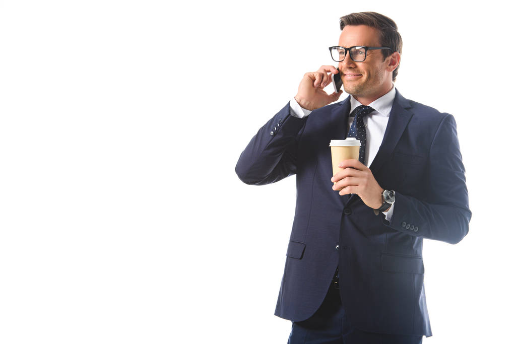 šťastný, podnikatel v brýlích mluví na smartphone a držení papíru šálek kávy izolovaných na bílém pozadí  - Fotografie, Obrázek